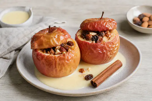 Zwei gebackene Bratäpfel mit Rosinen-Mandel-Füllung und Zimt, mit Vanillesauce auf einem Teller