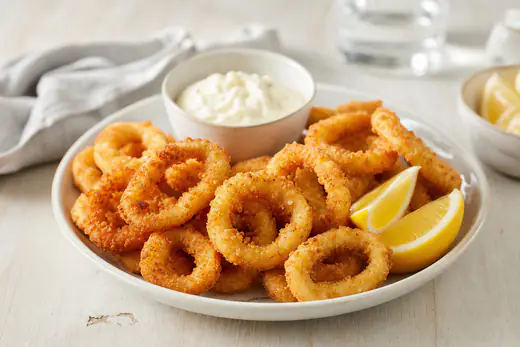 Goldbraun panierte Calamari-Ringe auf einem Teller mit Zitronenspalten und einem kleinen Schälchen Knoblauchmayonnaise