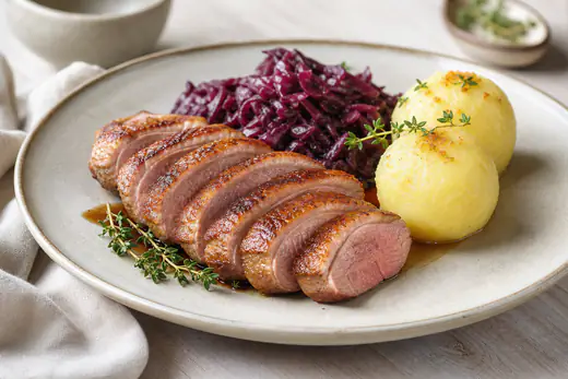 Aufgeschnittene rosa gebratene Entenbrust mit knuspriger Haut, dazu Rotkohl und Kartoffelklöße und Thymian
