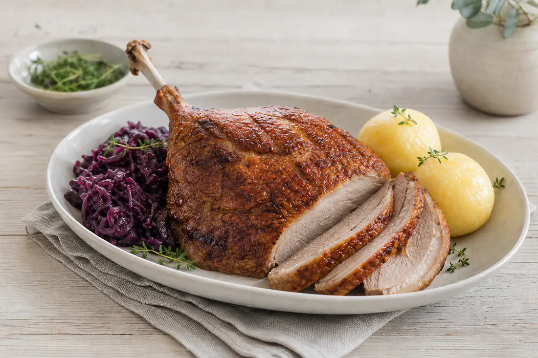Gebratene Gänsebrust mit Knochen und goldbrauner knuspriger Haut, in Scheiben geschnitten, dazu Rotkohl und Klöße
