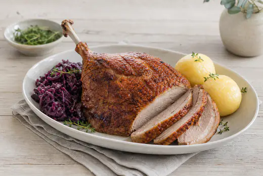Gebratene Gänsebrust mit Knochen und goldbrauner knuspriger Haut, in Scheiben geschnitten, dazu Rotkohl und Klöße