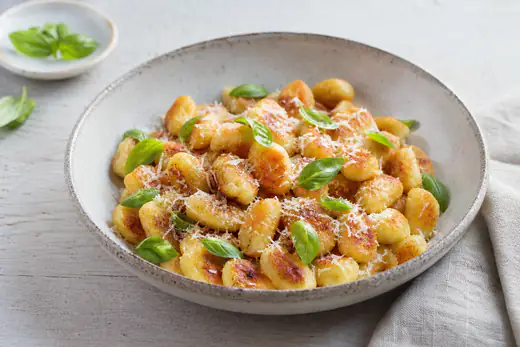 Goldbraun knusprige Gnocchi mit geriebenem Parmesan und frischen Basilikumblättern auf einem tiefen Keramikteller