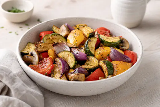 Buntes Grillgemüse aus Zucchinihalbmonden, roter und gelber Paprika, Rotzwiebelspalten und Champignonhälften in einer flachen Schüssel