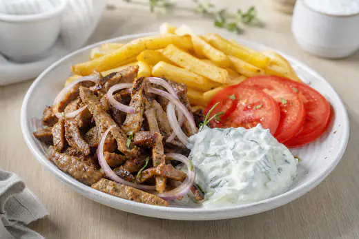 Knusprig gebratene Gyrosstreifen vom Schwein mit Zwiebelringen auf einem Teller, dazu Tzatziki, Tomatenscheiben und Pommes