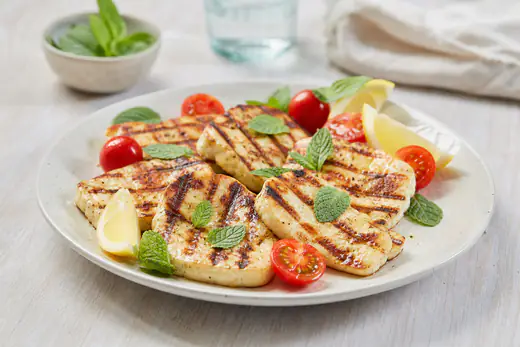 Goldbraun gegarte Halloumi-Scheiben mit Grillstreifen auf einem Teller, dazu Zitronenspalten, Kirschtomaten und frische Minze