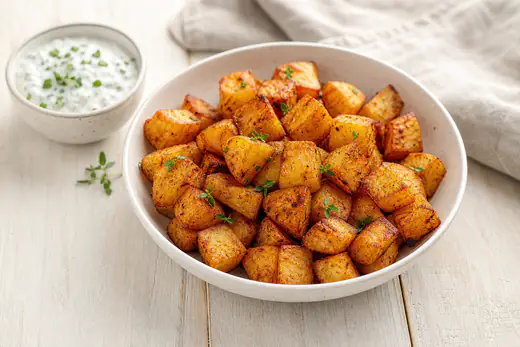 Goldbraune knusprige Kartoffelwürfel mit Paprikagewürz in einer weißen Schüssel, daneben ein Schälchen Kräuterquark