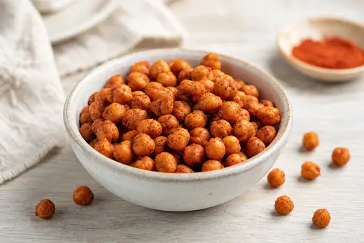 Knusprig geröstete Kichererbsen mit Räucherpaprika-Gewürz in einer kleinen Schüssel, einige verstreut auf dem Tisch