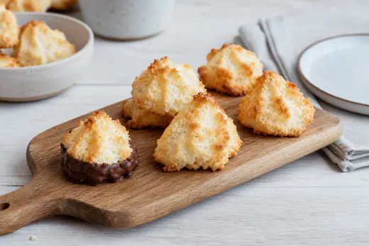 Kleine Kokosmakronen mit goldbraunen Spitzen, eine mit Schokoladenboden, auf einem Holzbrett