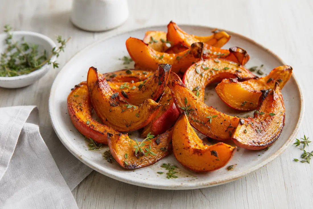 Knusprig geröstete Hokkaido-Kürbisspalten mit orangefarbener Schale und karamellisierten Rändern, mit Thymian auf einem Teller
