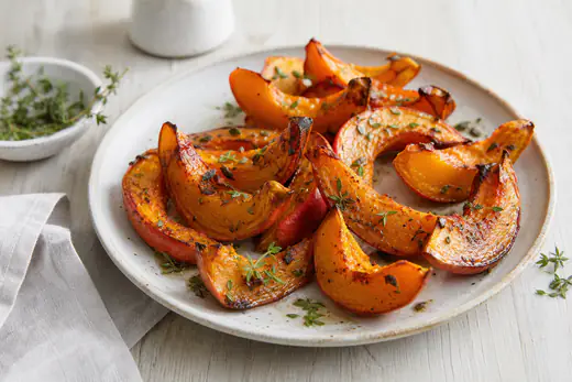 Knusprig geröstete Hokkaido-Kürbisspalten mit orangefarbener Schale und karamellisierten Rändern, mit Thymian auf einem Teller