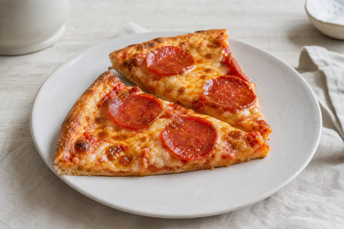 Zwei aufgewärmte Pizzastücke mit Salami und geschmolzenem Käse und knusprigem Rand auf einem Teller