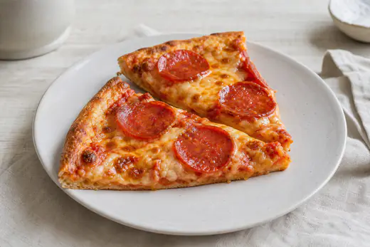 Zwei aufgewärmte Pizzastücke mit Salami und geschmolzenem Käse und knusprigem Rand auf einem Teller
