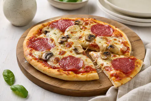 Kleine runde Pizza mit Mozzarella, Salami und Champignons und goldenem Rand auf einem Holzbrett, ein Stück leicht abgezogen