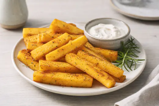 Goldgelbe knusprige Polenta-Pommes in länglichen Stiften auf einem Teller, mit einem kleinen Schälchen Dip und Rosmarin