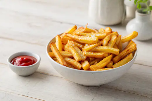Selbstgemachte goldgelbe Pommes frites aus frischen Kartoffeln, gesalzen in einer Schüssel, dazu ein Schälchen Ketchup