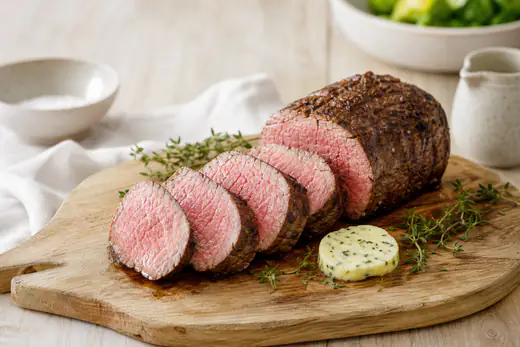 Gebratenes Rinderfilet in dicke Scheiben geschnitten, mit gleichmäßig rosa Kern, auf einem Holzbrett mit Thymian und Butter