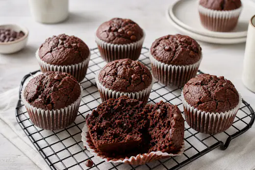 Dunkle Schokoladenmuffins mit Schokostückchen in Papierförmchen auf einem Abkühlgitter, einer in der Mitte durchgebrochen