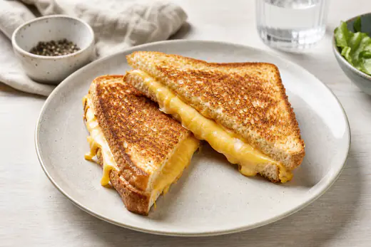 Zwei goldbraune Käsetoasts, diagonal halbiert, mit am Rand herausquellendem geschmolzenem Käse auf einem Teller
