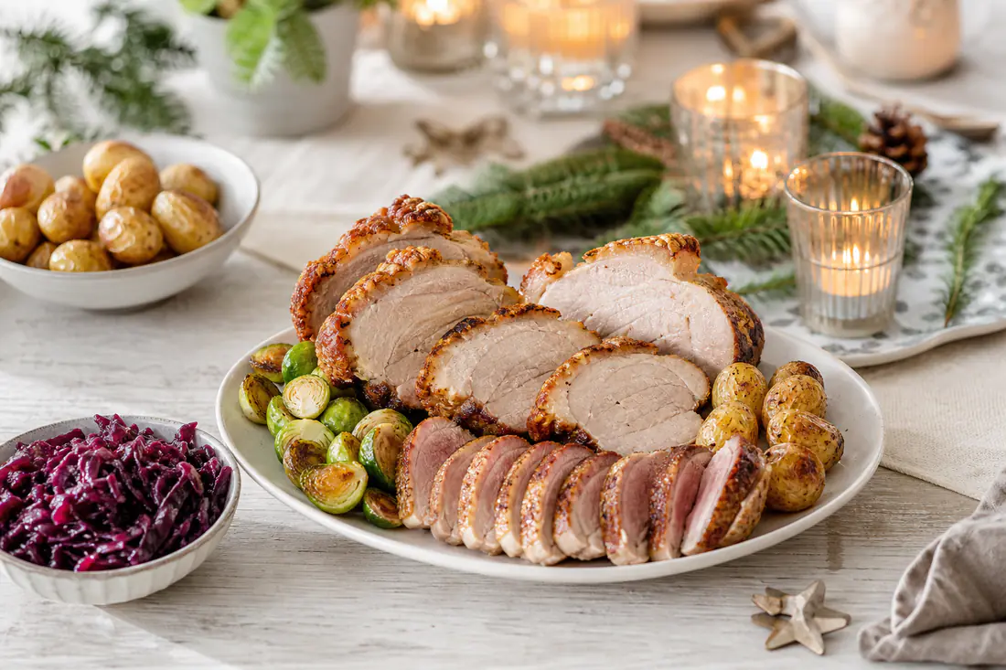 Festlich gedeckter Tisch mit Scheiben von Krustenbraten, Entenbrust, Rosenkohl, Rotkohl und Kartoffeln